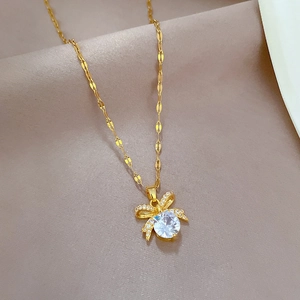 Luxurious gold stainless steel bow pendant necklace with sparkling crystal inlay on beige fabric