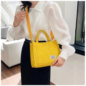 Detail of yellow corduroy handbag featuring a front pocket and soft textured fabric surface