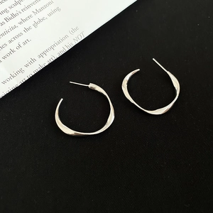 Detail of silver twisted C-shaped earrings with polished finish on a dark artistic background