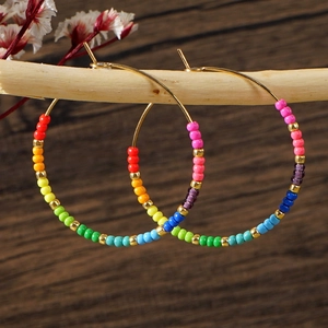 Close-up of rainbow seed beads on gold hoop earrings hanging on a light wooden stick