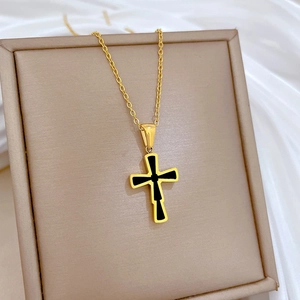 Detail view of a gold cross pendant necklace featuring a black center inlay on beige gift box