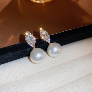 Close-up of geometric pearl earrings with marquise-cut zircon and golden finish