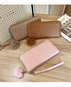 Three long zip wallets with V-shaped quilting and matching pompom charms on wood surface