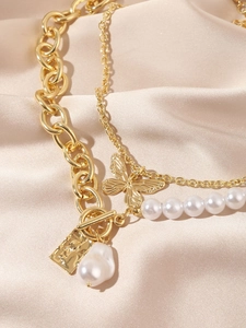 Close-up of layered gold chain necklace featuring baroque pearl and butterfly charm