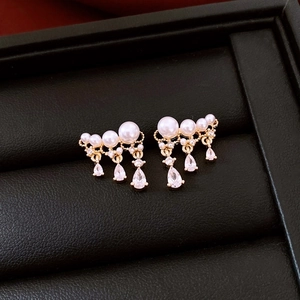 Close-up of gold drop earrings with white pearls and zircon on a black leather display