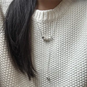 Detail of silver Y-shaped beaded necklace worn over a white knitted sweater