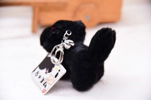 Detail of black plush cat keychain with silver bell and cartoon illustration tag