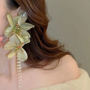 Close-up of oversized light green fabric flower earrings with beaded tassels on model