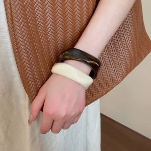 Detail view of acrylic tortoise shell and cream wide bangles worn on wrist with woven bag