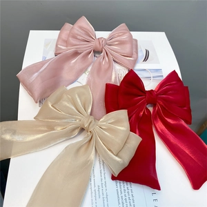 Three oversized layered bow hair clips in pink, gold and red with long flowing ribbons