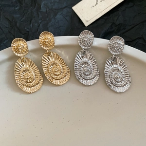 Detailed view of gold and silver spiral textured metal earrings on a white ceramic tray