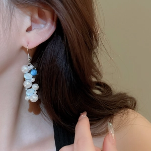 Detailed view of elegant pearl drop earrings featuring blue stones on model's ear