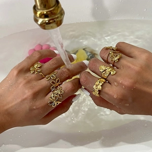 Waterproof gold-plated floral and butterfly rings shown under running water on a hand