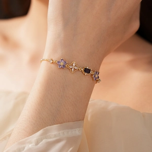 Detail view of gold flower bracelet with purple petals and deep blue gemstone