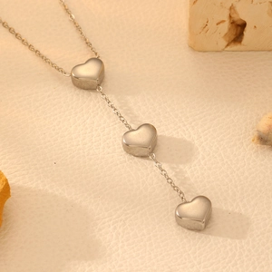 Détail macro de trois pendentifs cœur lisses sur une fine chaîne en acier inoxydable argenté