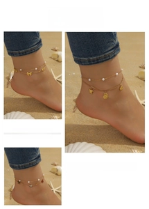 Detail of gold layered anklets with starfish, shell, and butterfly charms on beach sand