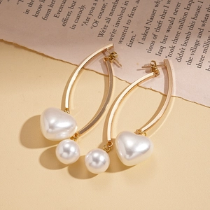 Boucles d'oreilles dorées vintage avec pendentifs cœur et perle sur fond de vieux journal