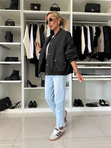 Close-up of black quilted baseball jacket with ribbed cuffs and large pockets on female model