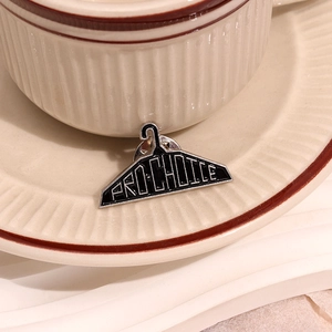 Black hanger shape enamel brooch with Pro-Choice text on a ceramic plate background