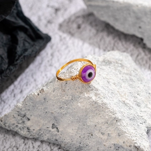 Macro shot of handmade gold wire-wrapped ring with purple evil eye bead on white stone