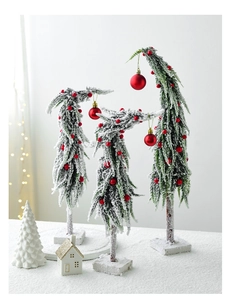 Close-up of three snowy mini Christmas trees with red balls on a white desktop scene