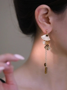 Gros plan de boucles d'oreilles feuilles de ginkgo dorées avec franges et perles œil de tigre