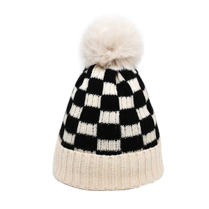 Close-up of winter knit beanie with black and white checkerboard pattern and plush pompom