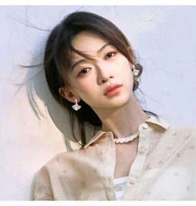 Detail of ginkgo leaf pearl earring worn by a model against a textured wall background