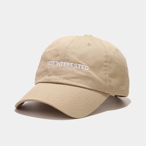 Detail of light khaki baseball cap with white NOT INTERESTED embroidery on cotton fabric