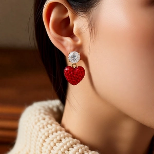 Gros plan d'une boucle d'oreille cœur rouge avec zircon sur base dorée portée sur l'oreille