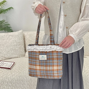 Lace trim detail on a blue and brown plaid tote bag held in a cozy home setting