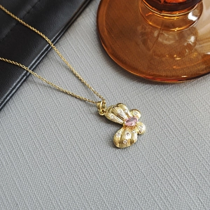 Detail of a golden butterfly pendant featuring a pink drop-shaped gemstone and white zircons