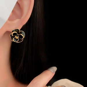 Macro close-up of a vintage black and gold camellia flower earring worn on a model's ear