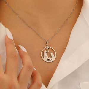 Close-up of a silver hollow Nativity pendant necklace worn on a model's collarbone
