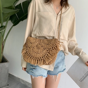 Handmade woven straw crossbody bag with fringe detail shown on a fashion model