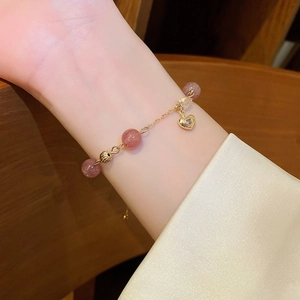 Detail of pink strawberry crystal heart bracelet with gold chain on a female wrist