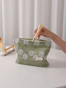 Green linen cosmetic bag with white floral embroidery and zipper closure held by hand