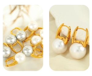 Detail of gold pearl huggie earrings featuring white and silver-grey pearls on soft fabric