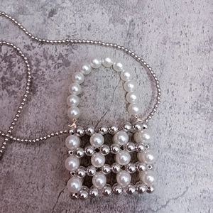 Close-up of woven mini bag with white pearls, silver beads, and round bead chain strap