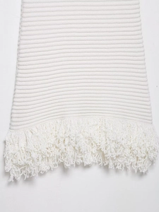 Detailed close-up of white knitted fabric texture and elegant fringe hem on the dress