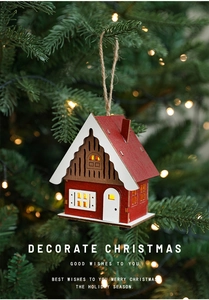 Hanging wooden LED Christmas house with red walls and warm glowing lights on a pine tree