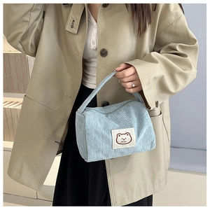 Detail of light blue corduroy handbag with cute bear patch held by a model