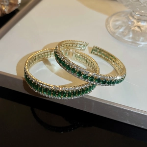 Close-up of golden open bangles with emerald square stones and sparkling white zircons