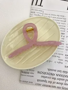 Pale pink translucent resin hair claw clip with golden spring on ceramic plate