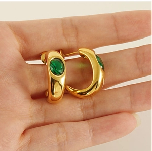 Detail of gold C-shaped earrings featuring a green oval zircon gemstone in a hand-held shot