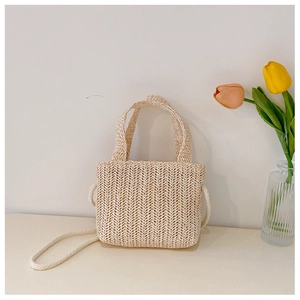 Detail of small beige woven straw tote bag with handles and shoulder strap near tulips