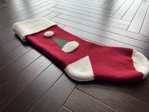 Top view of red and white knitted Christmas stocking with green hat pattern on wood floor