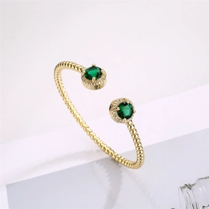 Detail of gold open bracelet featuring emerald green gemstones and sparkling accents