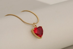 Detail of red heart crystal pendant with gold snake chain on textured background
