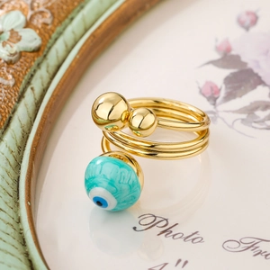 Macro detail of gold-plated spiral ring featuring turquoise evil eye bead and golden spheres